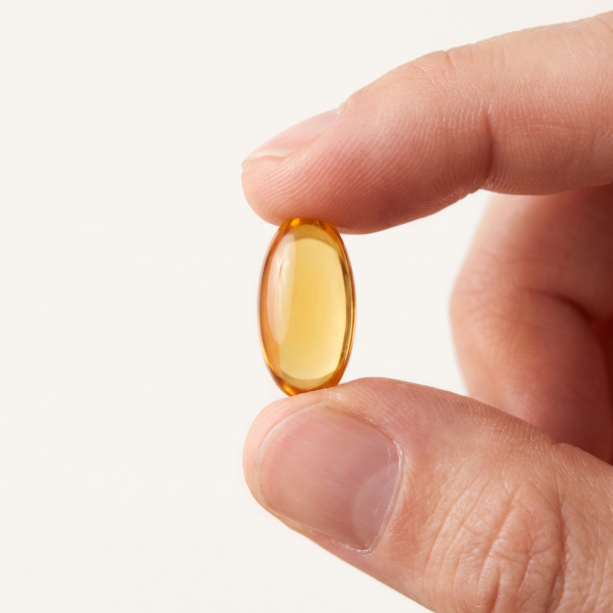 A single Omega XL softgel held between finger and thumb for scale