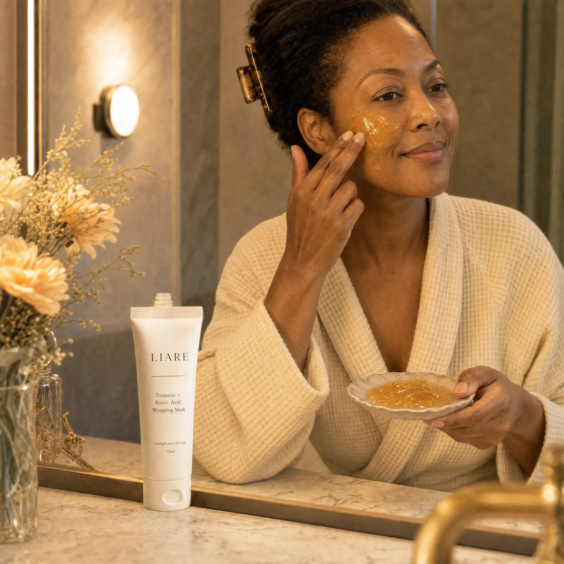 Woman in her 50s applying a thin layer of the golden wrapping mask to her cheek before bed